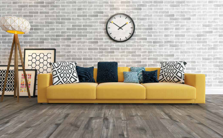 Living room with yellow couch, pillows, and clock on brick wall. Modern home interior design.