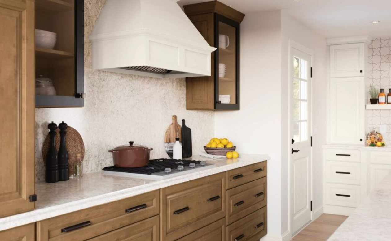 Farmhouse kitchen with wood and white cabinets, cream range hood, gas stovetop, cutting boards, lemons, and potted plants.