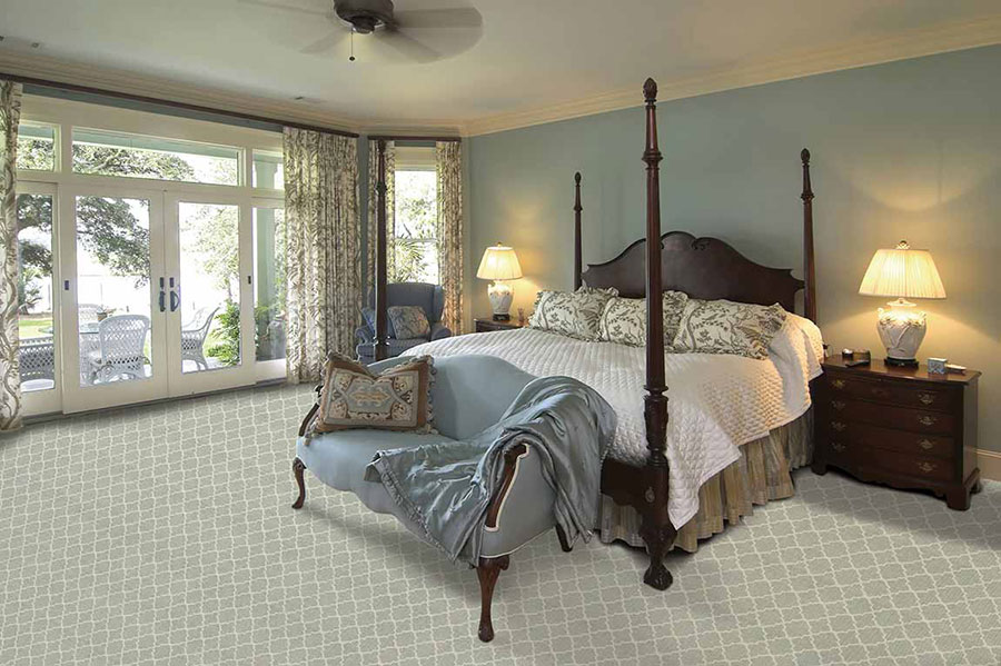 Bedroom furnished with a large four post canopy bed and two dark-stained wood nightstands on with lamps and patterned carpet.