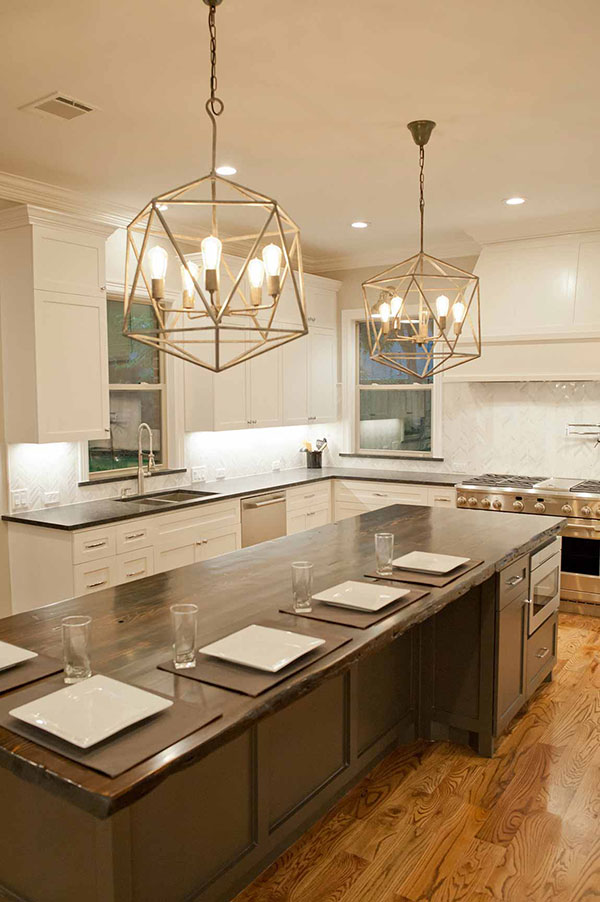 Kitchen with white cabinets, a large island with wood top and bar-style seating, and modern chandeliers.
