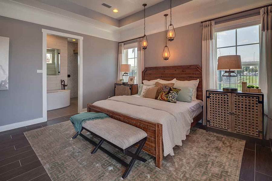Bedroom decorated with a bed on a wood frame, lamps on large nightstands, a ceiling mounted pendant lights, and recessed lighting on dark brown luxury vinyl plank flooring.