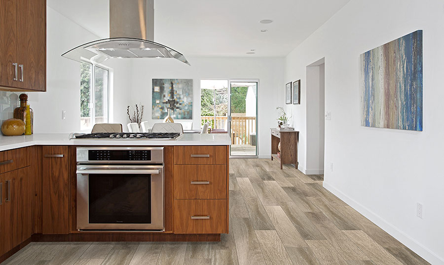 A modern open kitchen with natural wood finished cabinets and white countertops on wide strip luxury vinyl floors.
