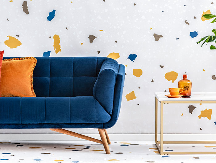 Modern blue loveseat with orange throw pillows and customizable Memphis design inspired wallpaper and flooring.