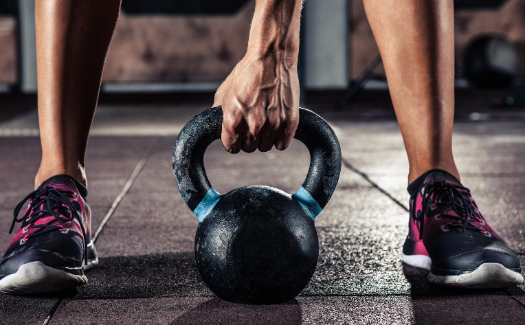 Person grasping kettlebell standing on rubber flooring